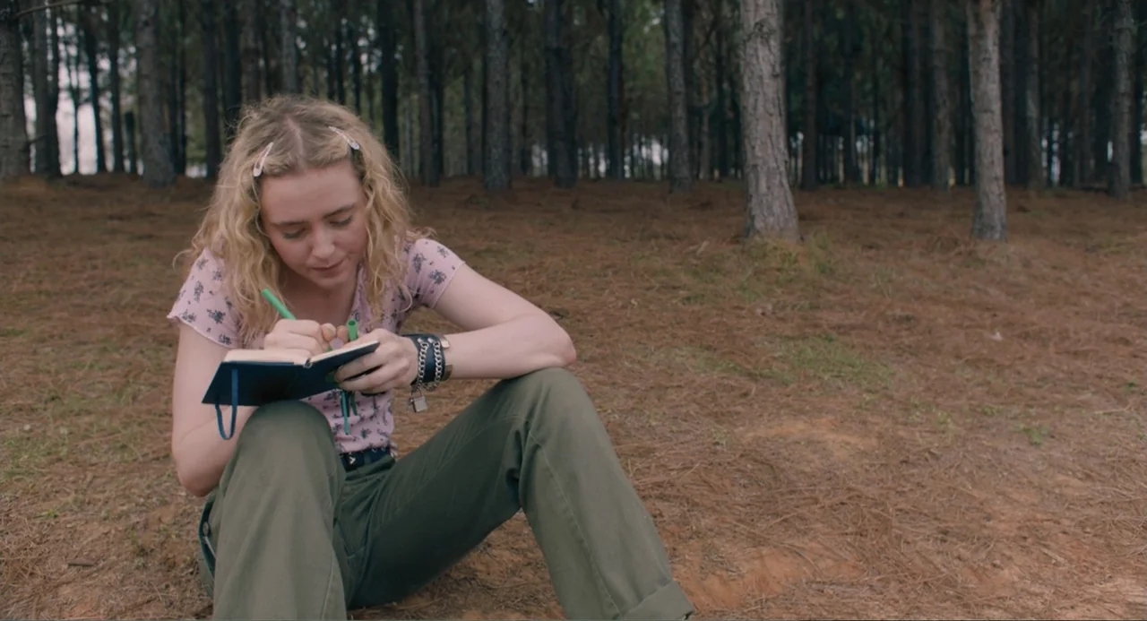 The Map of Tiny Perfect Things (2021) movie still: medium — A dense grove of thin pine trees covers the dry, needle-strewn ground. A young woman in…