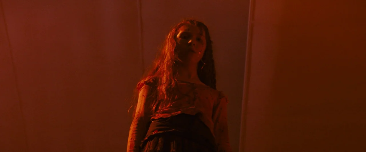 Don’t Breathe 2 (2021) movie still: medium — A dimly lit room is bathed in a deep, saturated red wash of light. A young girl with long, wavy auburn…