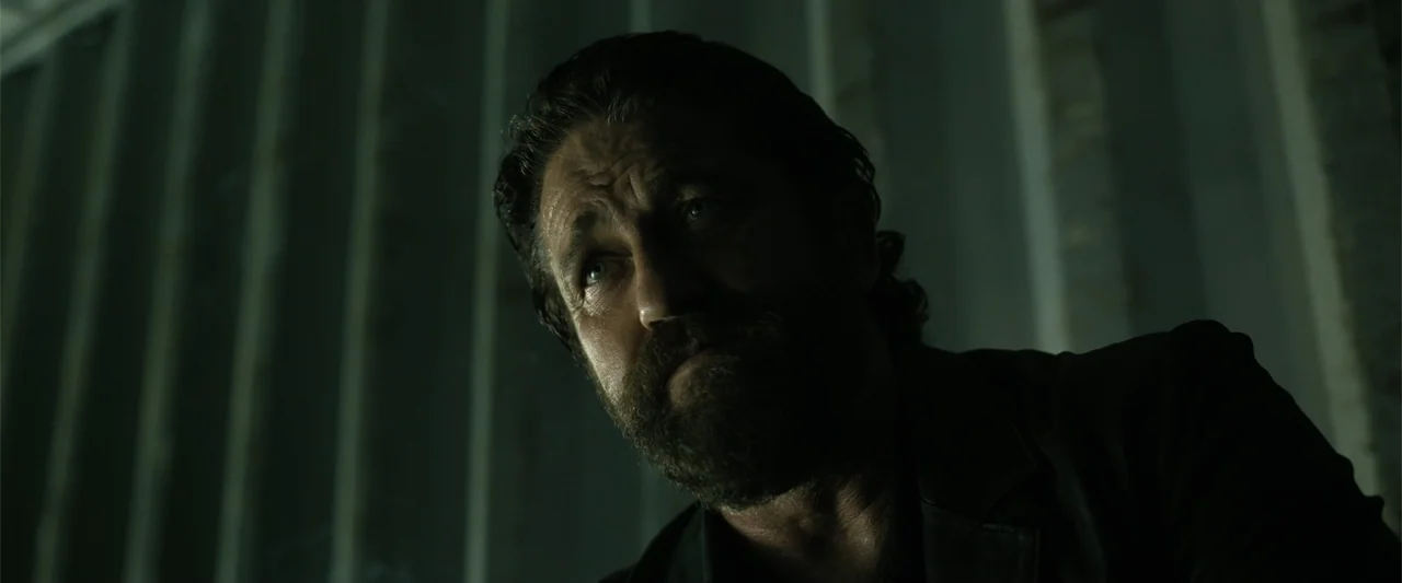 Den of Thieves 2: Pantera (2025) movie still: closeup — A dark industrial interior features vertical metal wall studs in the background. A man with…