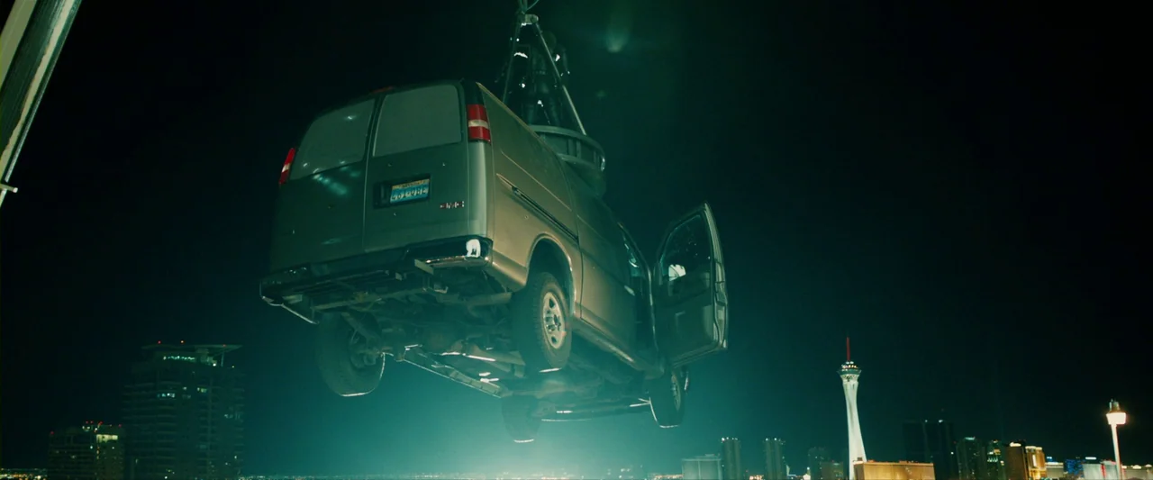 The Last Stand (2013) movie still: wide — A silver GMC van hangs suspended in the dark night air above a city. Below it, the distant lights of a…