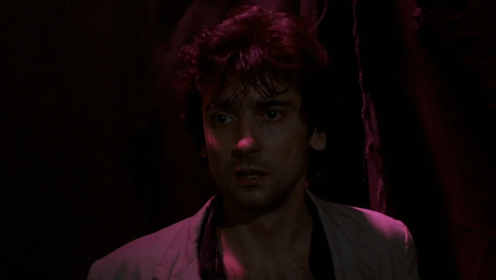 After Hours (1985) movie still: medium — A dark, minimally lit space with heavy shadows obscuring the surrounding environment. A man stands in the…