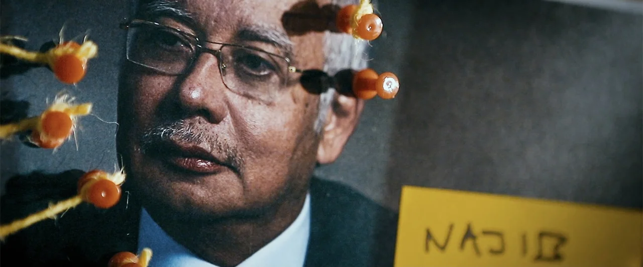 The Kleptocrats (2018) movie still: closeup — An interior space features an older man's portrait displayed behind a glass board. Small orange pins…