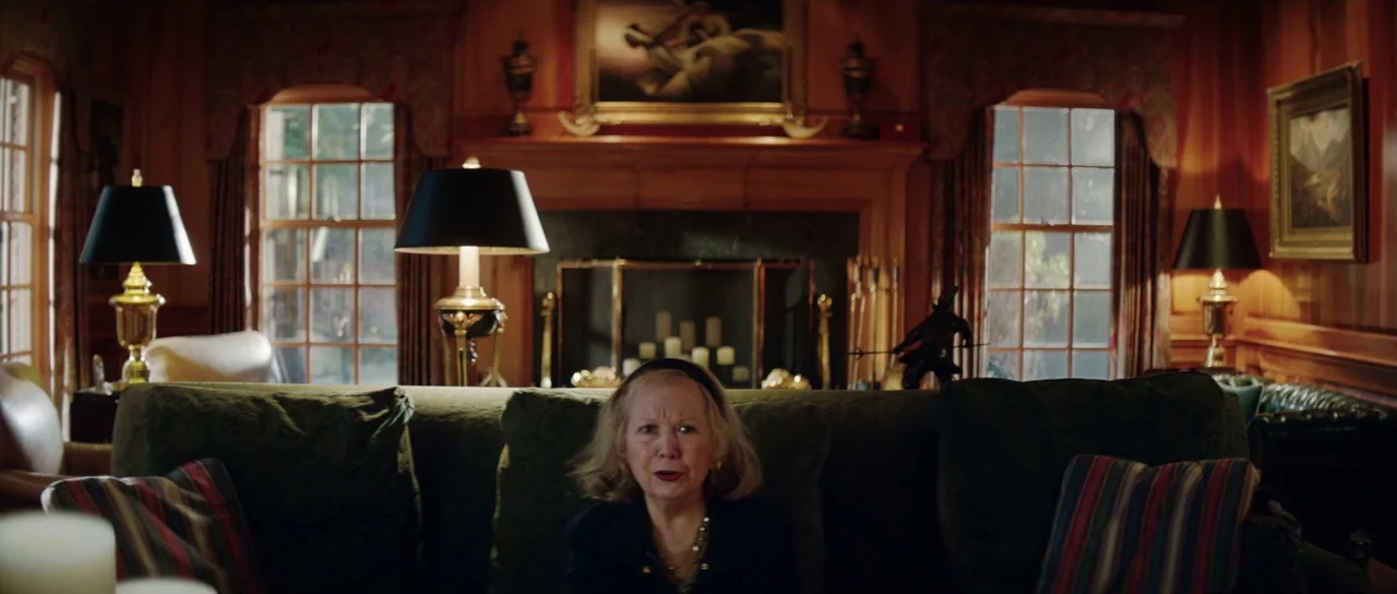 American Animals (2018) movie still: medium — A traditional living room features wooden wall paneling, a stone fireplace, and green furniture. An…