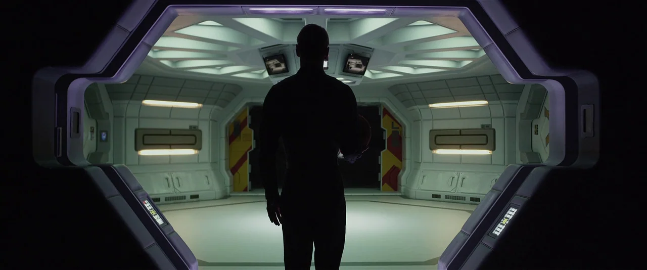 Prometheus (2012) movie still: fullbody — A stark white modular spaceship interior features geometric panels and hexagonal door frames. A person…