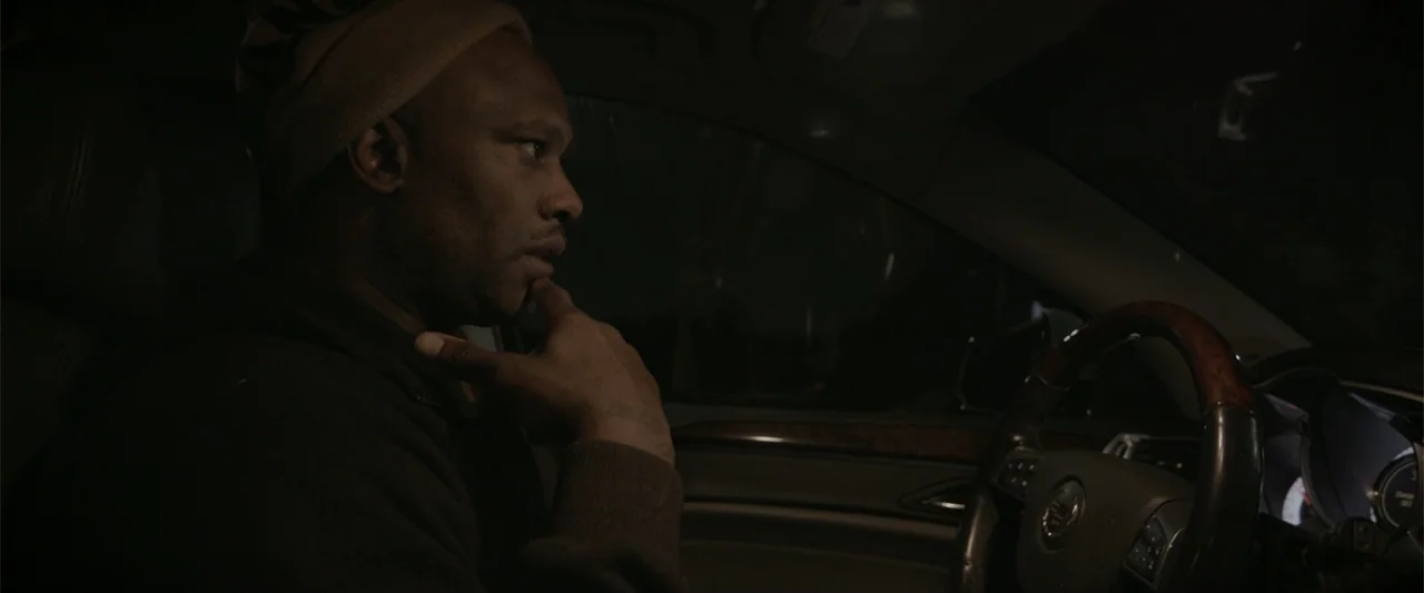 Maxine's Baby: The Tyler Perry Story (2023) movie still: medium — The interior of a modern car at night is dark and dimly lit. A man in a brown…