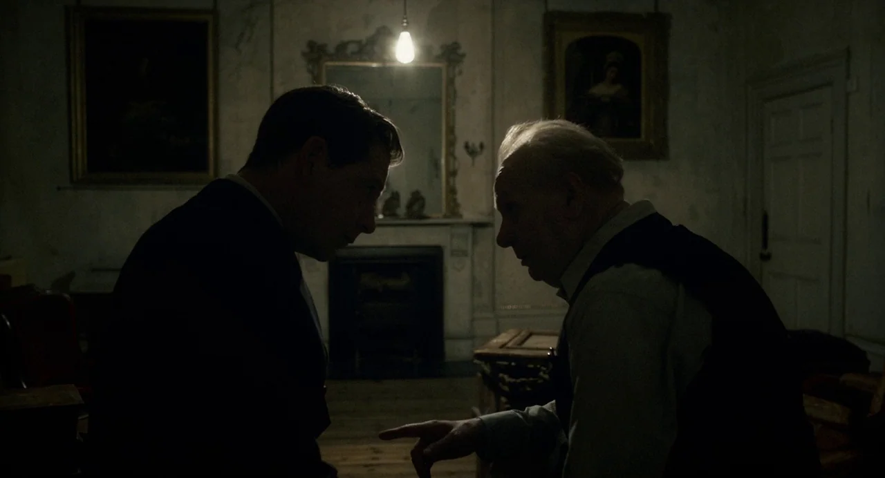 Darkest Hour (2017) movie still: medium — A dimly lit room contains two oil paintings on the wall above a fireplace. Two men stand in silhouette…