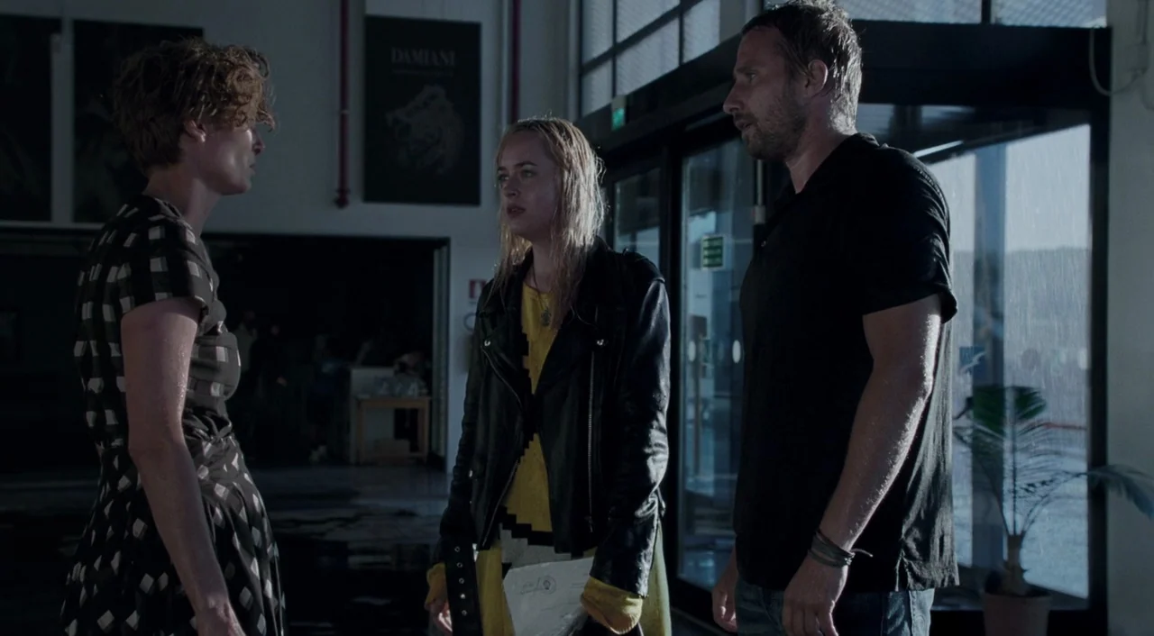 A Bigger Splash (2015) movie still: medium — A spacious, sparsely furnished lobby features high windows and concrete floors. Three individuals stand…