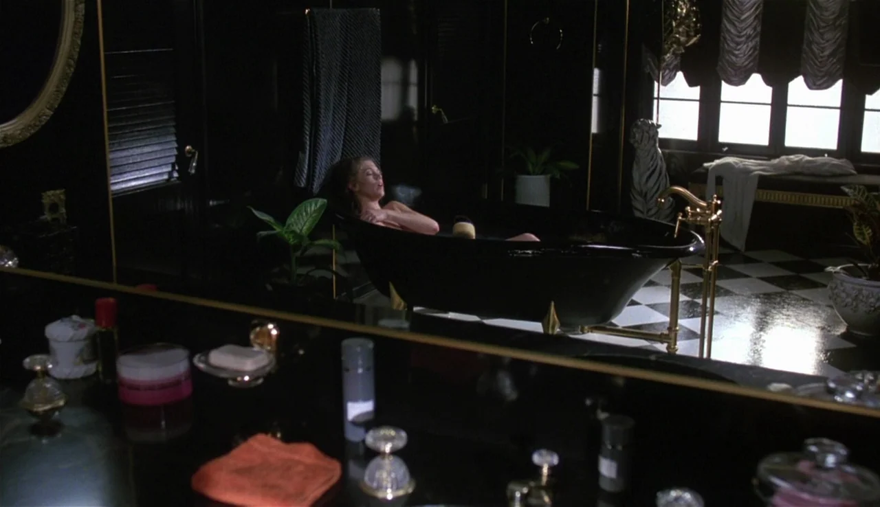 Body Heat (1981) movie still: wide — A spacious room features black walls, gold trim, and a high-contrast checkerboard tile floor. A woman relaxes…