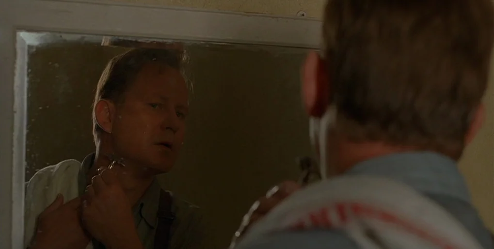 Dominion: Prequel to the Exorcist (2005) movie still: medium — A man in a pale shirt stands in a room with a mirror. He is shaving his face while…