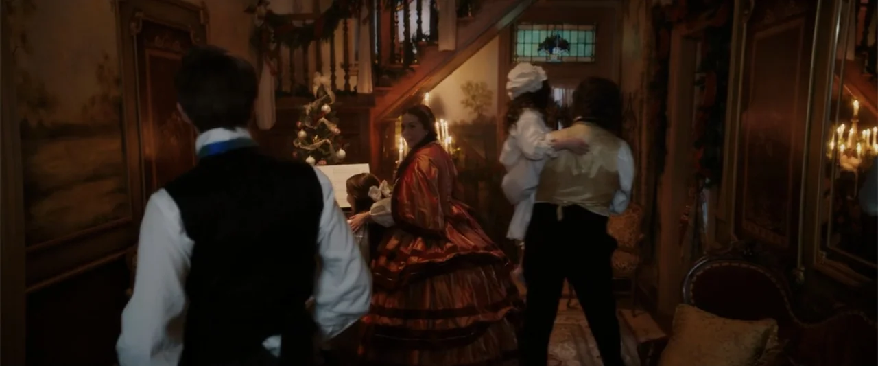 I Heard the Bells (2022) movie still: medium — A dark Victorian entrance hall features a wooden staircase and a small decorated tree. A family…