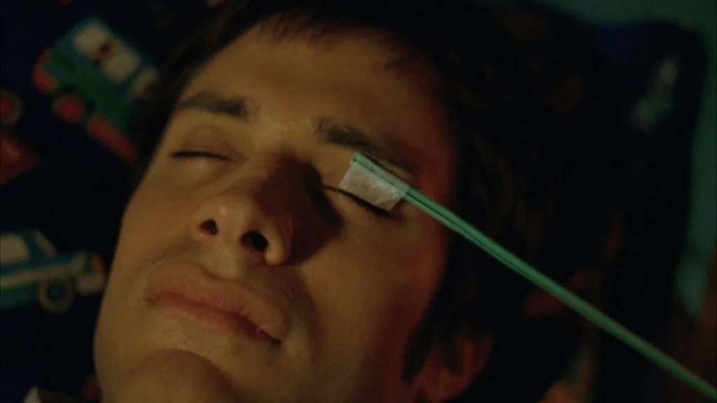 The Science Of Sleep (2006) movie still: closeup — A man lies on a pillow patterned with cartoon vehicles in a dark room. A thin, pale green plastic…