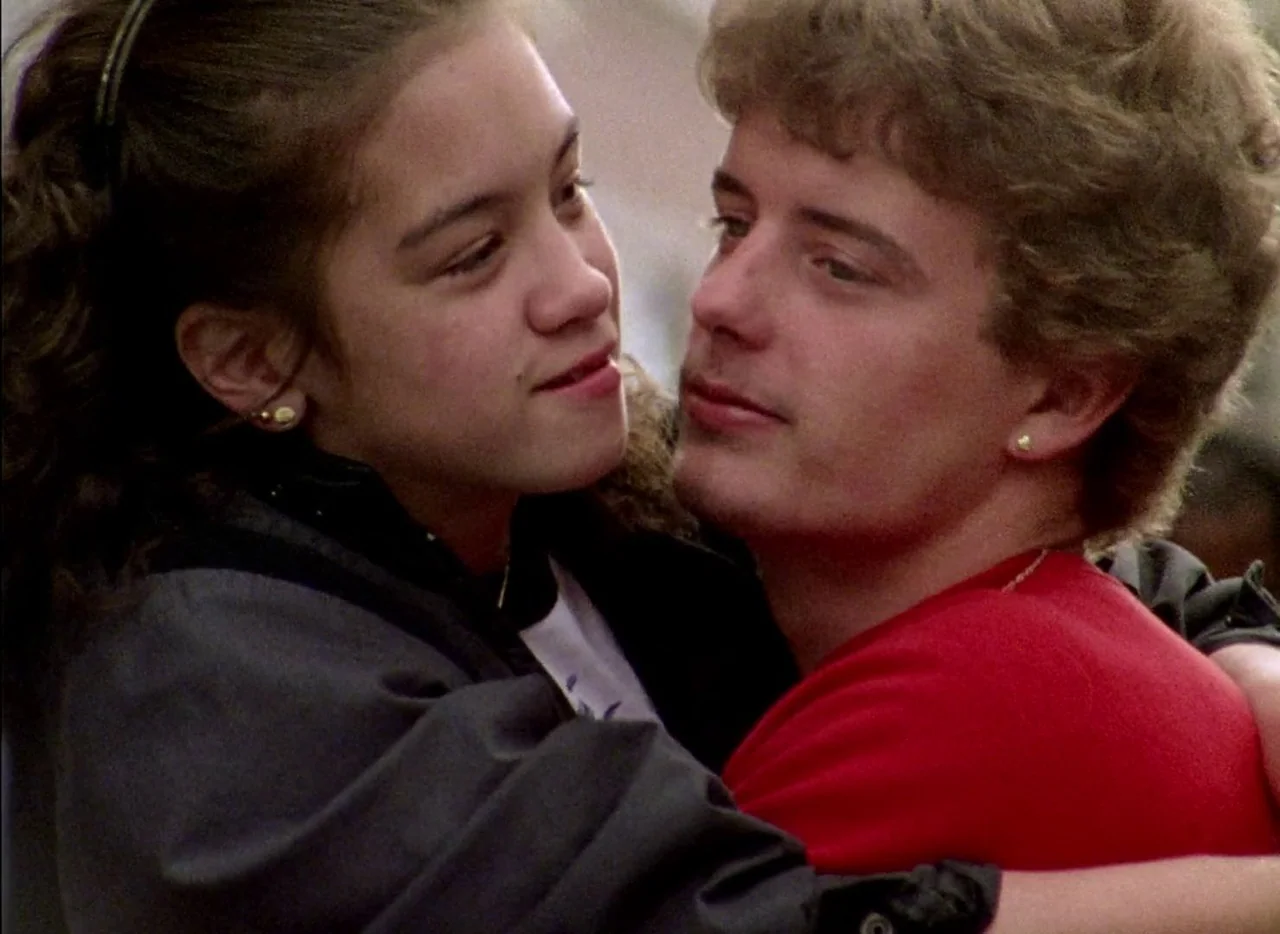 Streetwise (1984) movie still: closeup — A teenage couple stands close together in an outdoor area during the daytime. The pair embrace with the…