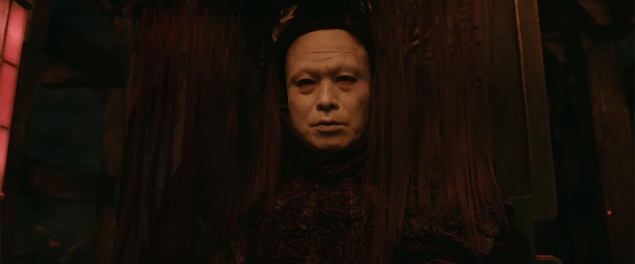 Along with the Gods: The Last 49 Days (2018) movie still: closeup — A dimly lit interior space with dark wood structures visible in the background.…