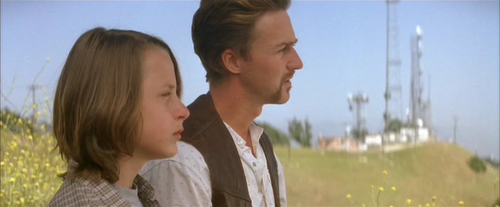Down In The Valley (2005) movie still: medium — A grassy hillside under a clear sky with several communication towers on the horizon. A young boy…