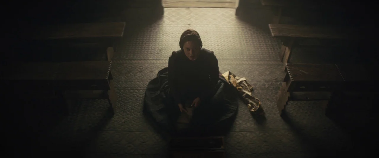 Macbeth (2015) movie still: wide — A stone-floored church interior features rows of simple wooden benches in dim light. A woman sits on the floor in…