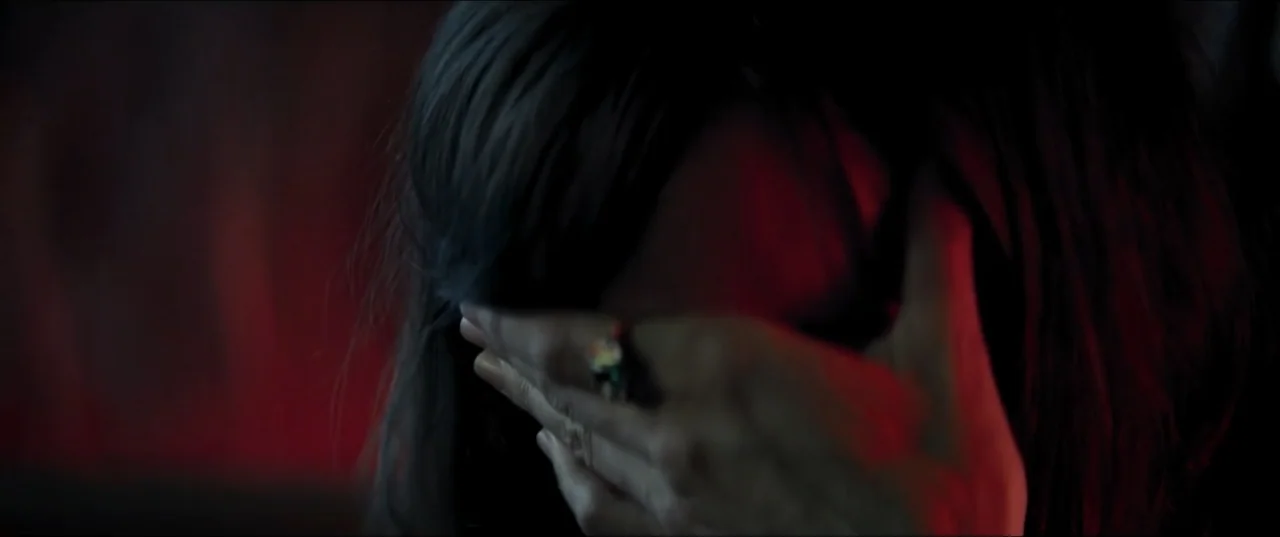 Offseason (2022) movie still: closeup — A dark indoor space with minimal detail and prominent red side lighting. A person reaches up with one hand…