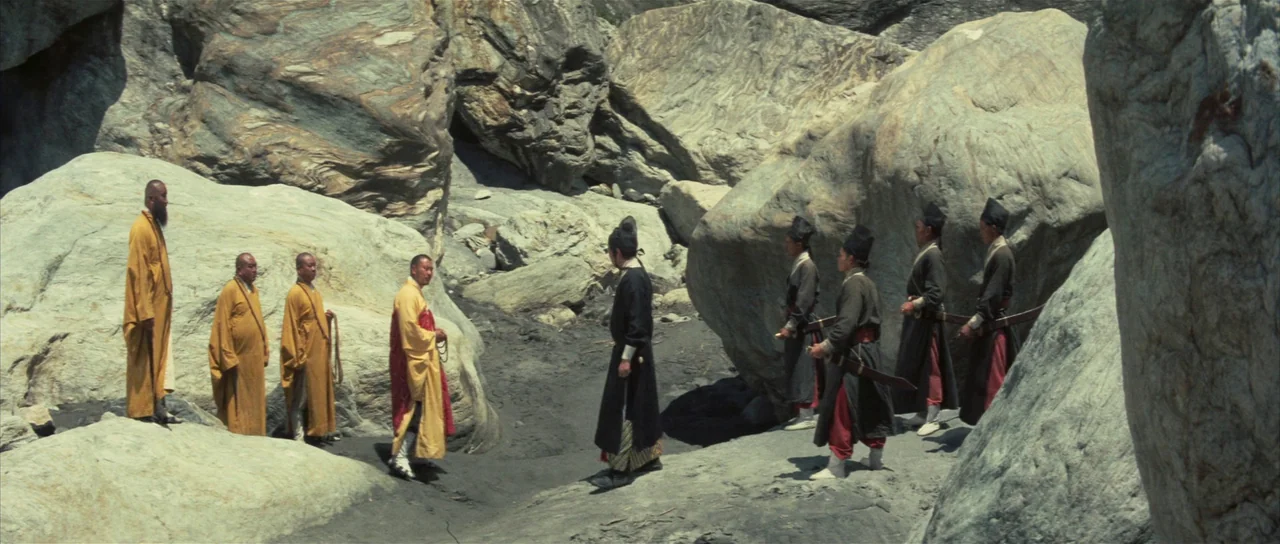A Touch of Zen (1971) movie still: wide — A dry desert canyon floor features large weathered grey boulders and smooth rock formations. Four monks in…