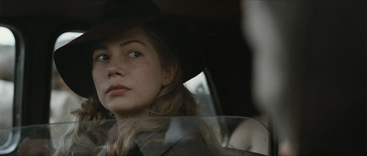 Suite Française (2015) movie still: closeup — A 1940s vehicle interior with window reflections showing the exterior. A woman in a hat sits in the…