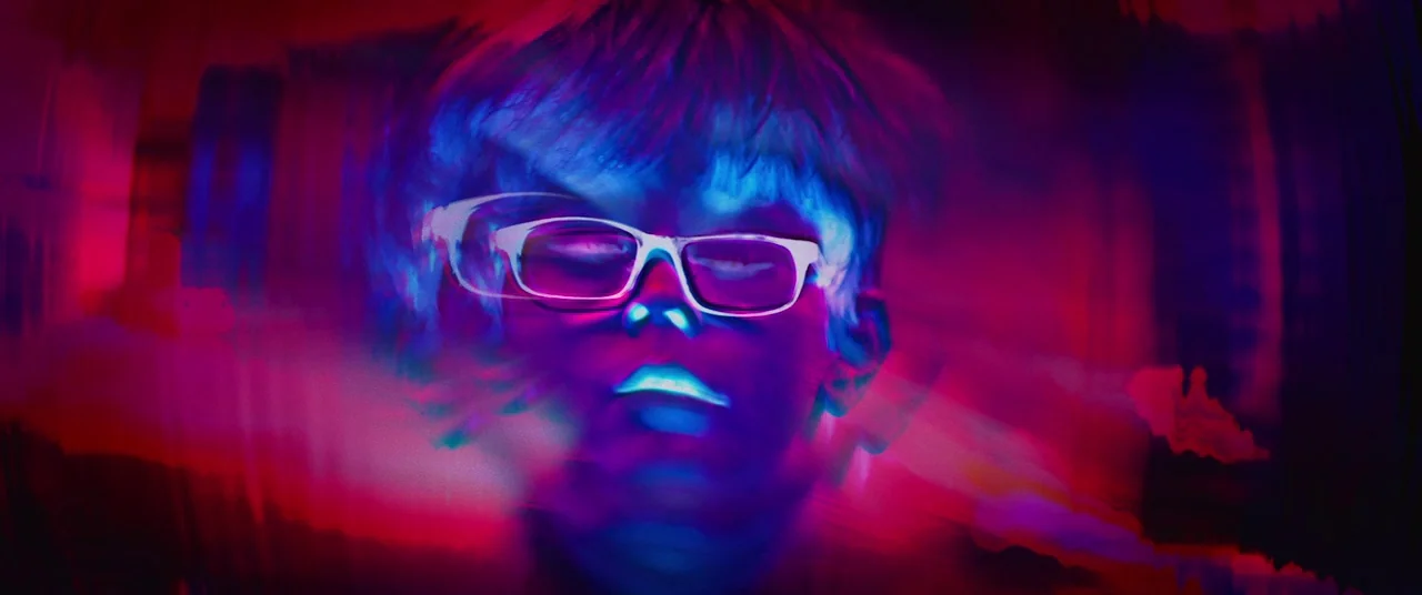 Colour Out of Space (2020) movie still: closeup — A person's face is centrally framed in a dark space filled with chromatic digital distortions. The…