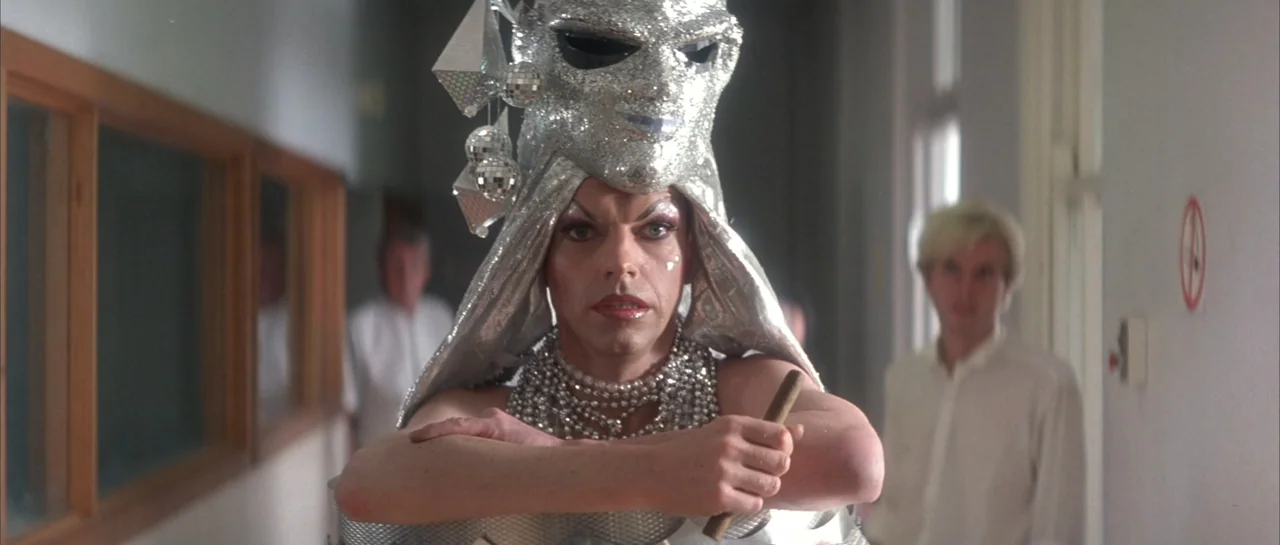 The Adventures of Priscilla, Queen of the Desert (1994) movie still: medium — A clinical corridor features pale walls, wood-framed windows, and an…