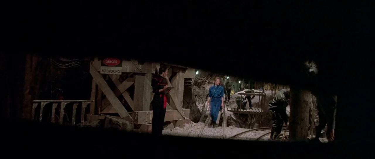 A View to a Kill (1985) movie still: wide — A subterranean mining tunnel features wooden support structures and a "Danger No Smoking" sign. Several…