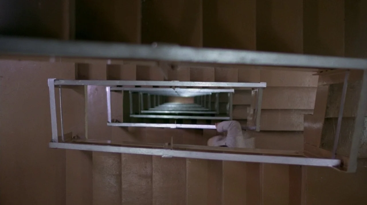 Thief (1981) movie still: wide — A vertical view down a concrete apartment building stairwell with metal handrail segments. The central open space…