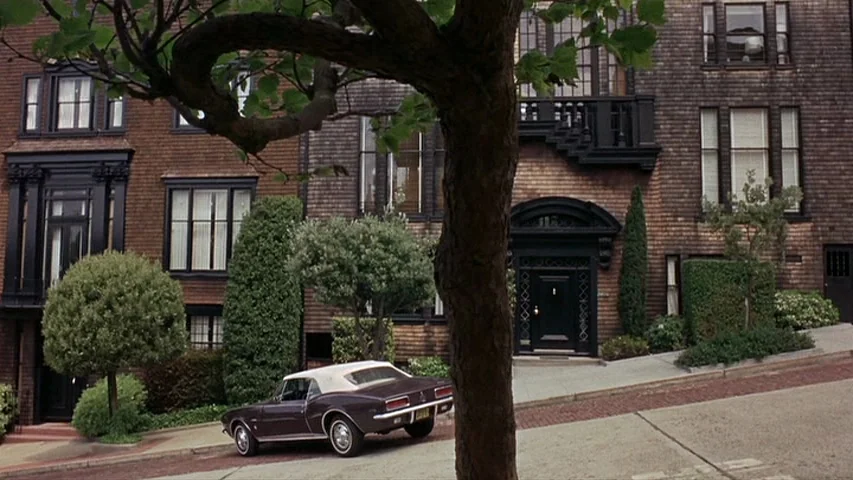 Petulia (1968) movie still: wide — A steeply sloped street features brown shingled townhouses with black architectural trim and windows. A…
