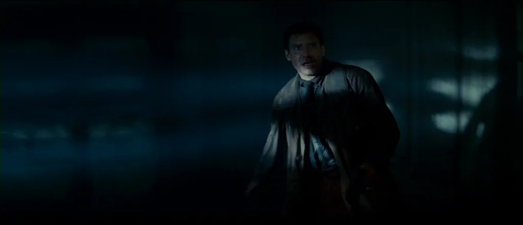 Blade Runner (1982) movie still: medium — A dimly lit industrial corridor with blue-toned shadows and obscured architectural details. A man in a tan…