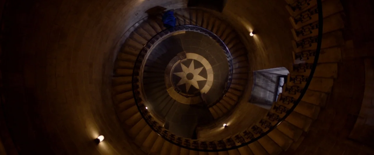Paddington 2 (2017) movie still: establishing — A stone spiral staircase descends toward a central floor medallion with a star design. Walls are…