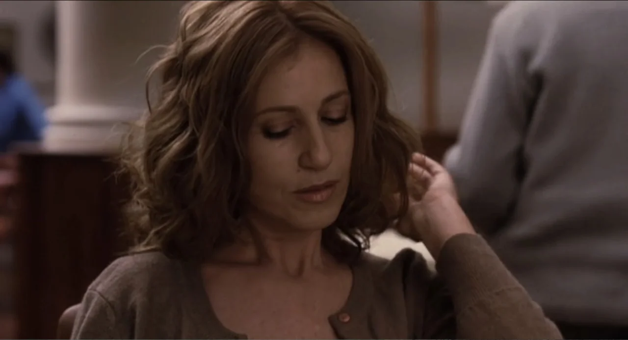 The Holy Girl (2004) movie still: closeup — A woman sits in a brightly lit indoor space with blurry figures in background. The woman with wavy brown…