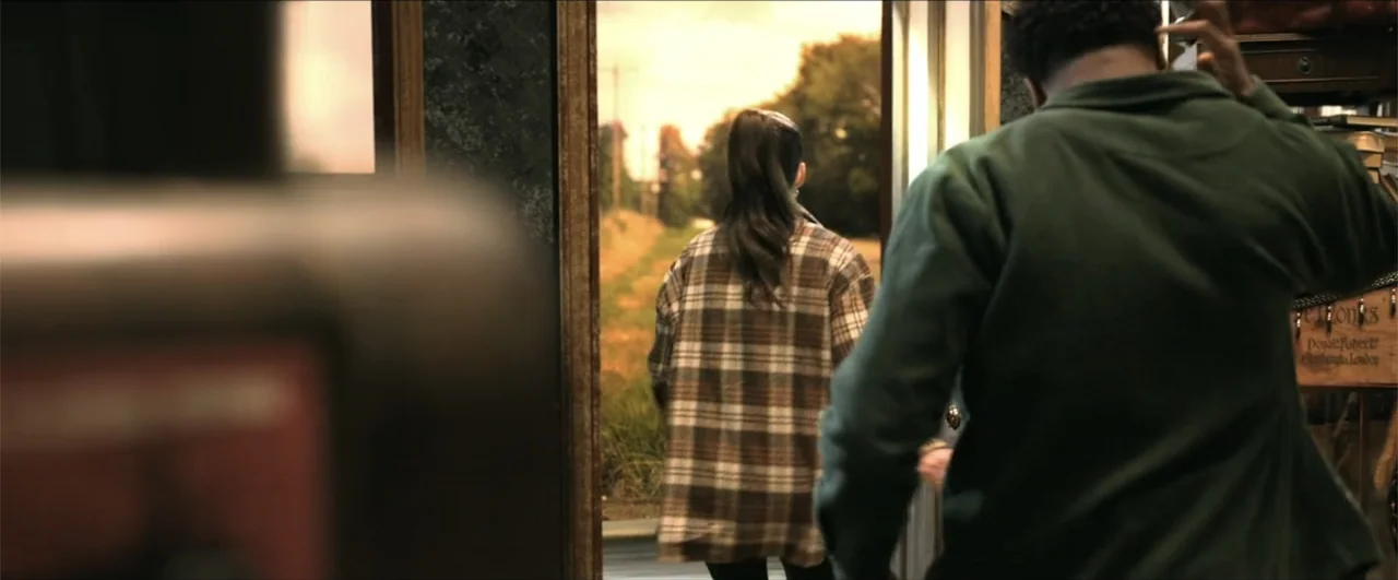 Jeepers Creepers: Reborn (2022) movie still: medium — A doorway frames a rural road bordered by trees under warm afternoon light. A man and a woman…