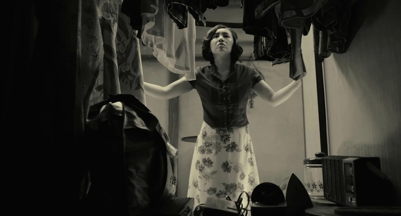 The Whispering Star (2015) movie still: medium — A small closet space is filled with hanging garments on both sides. A woman stands in the center…