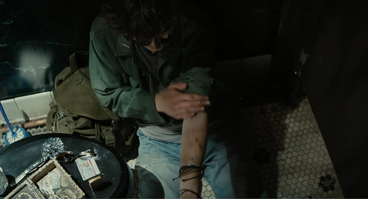 Beautiful Boy (2011) movie still: medium — A dimly lit tiled public restroom floor contains a backpack and drug paraphernalia. A person in a green…