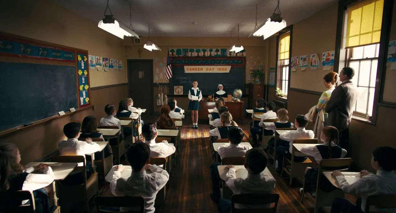 The Irishman (2019) movie still: wide — A 1960s school classroom features rows of wooden desks and a black chalkboard. A young female student stands…