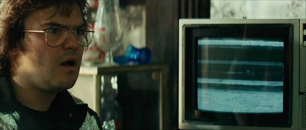 Be Kind Rewind (2008) movie still: medium — A cluttered room contains a man sitting beside an old television set. The television screen displays…