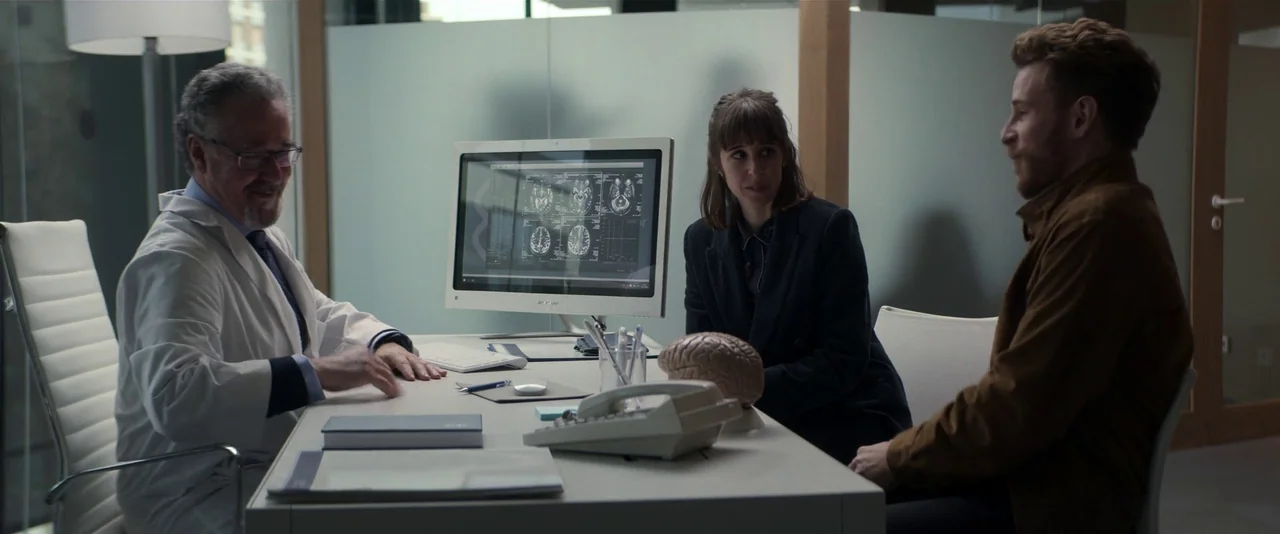 Crazy About Her (2021) movie still: wide — A modern medical consultation room features white desks and opaque glass partitions. A doctor sits across…