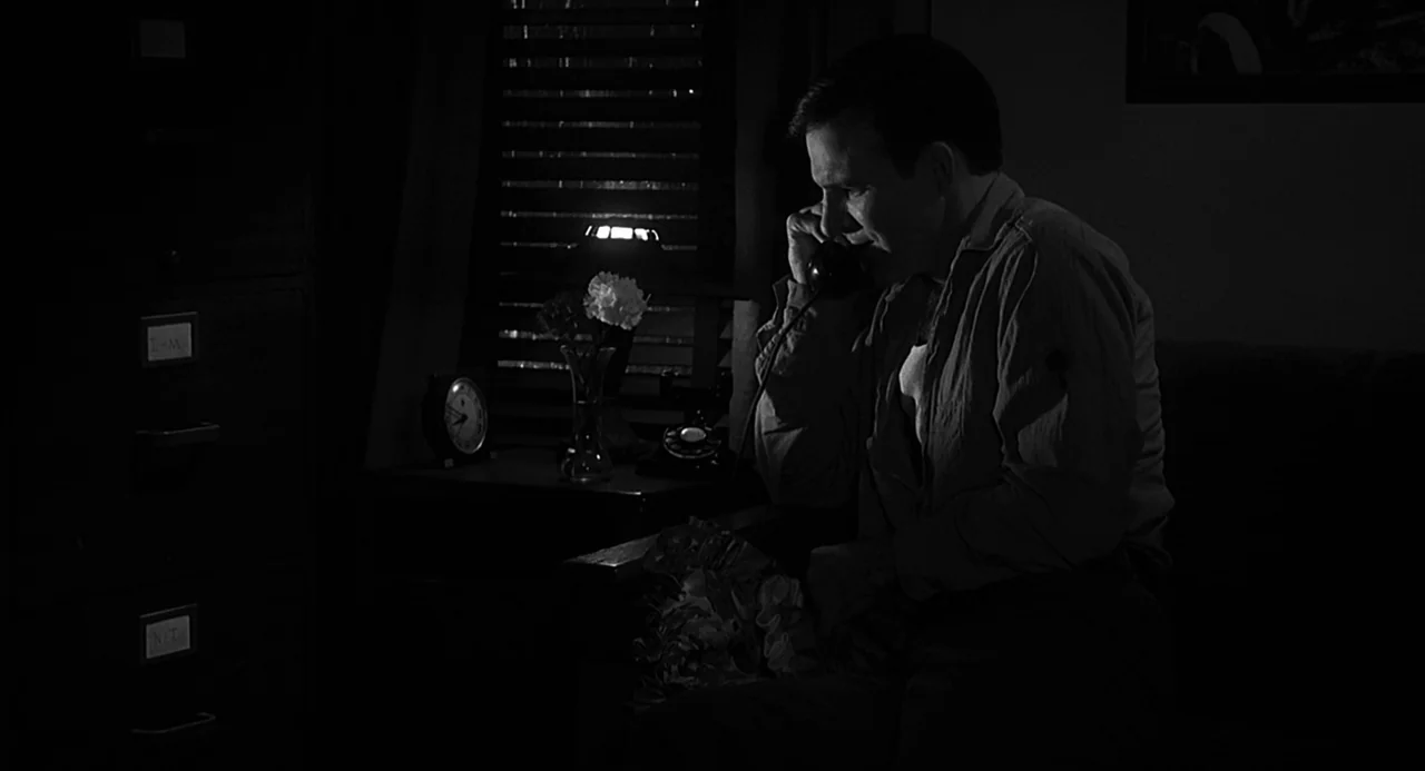 Dead Men Don’t Wear Plaid (1982) movie still: medium — A dimly lit room features a metal file cabinet and a desk with a telephone. A man sits in…