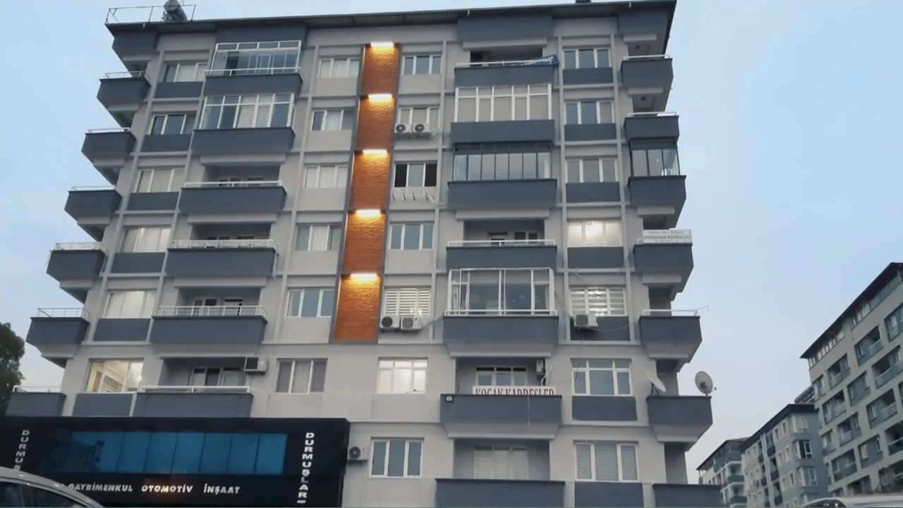 Death Without Mercy (2024) movie still: establishing — A modern multi-story apartment building features grey and white concrete balconies with glass…