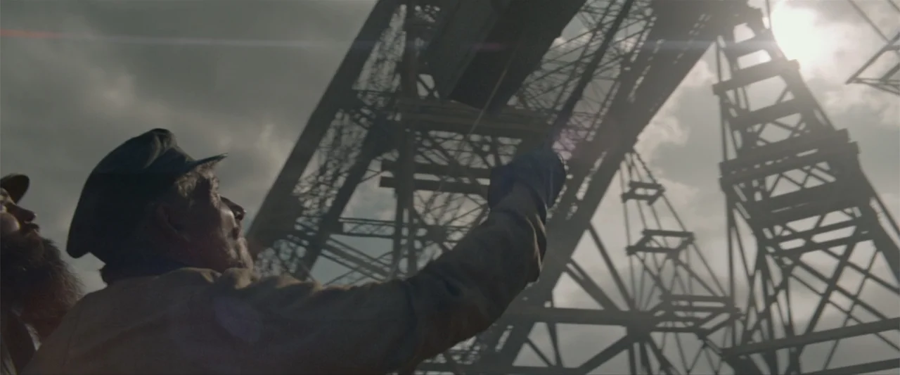 Eiffel (2021) movie still: medium — A high-angle view shows metal industrial trusses silhouetted against a bright, cloudy sky. Two men in work caps…