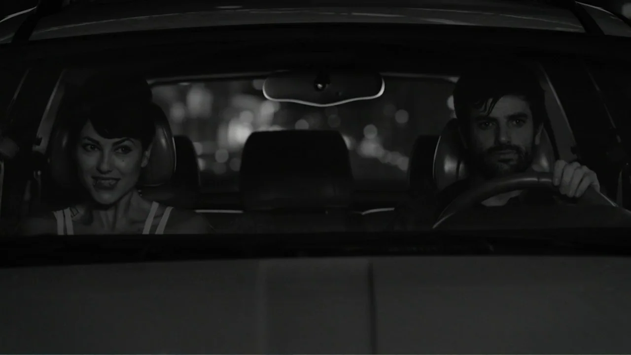 Alice in Marialand (2014) movie still: medium — A dark car interior at night shows a man and woman in the front seats. The man grips the steering…