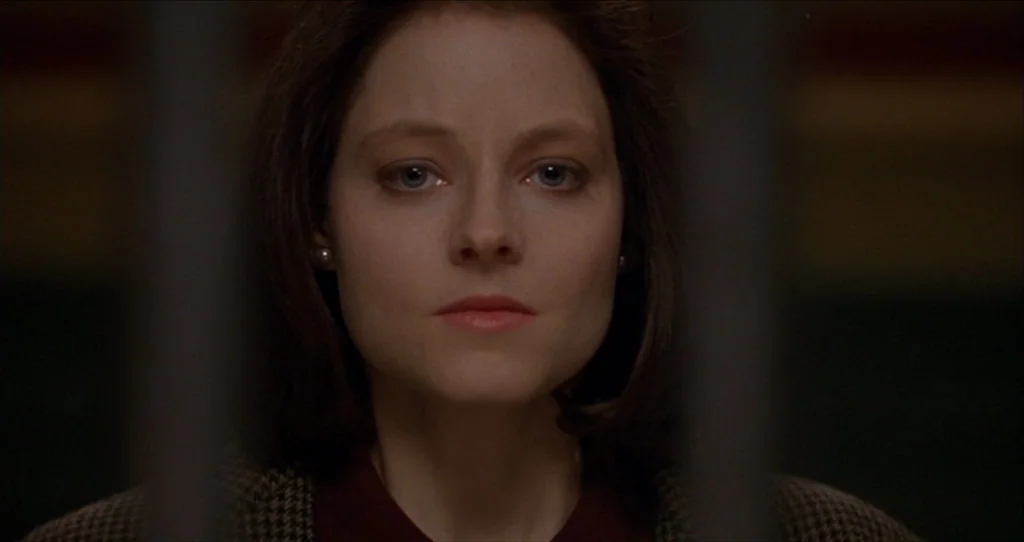 The Silence Of The Lambs (1991) movie still: closeup — A dark indoor space with vertical bars partially obscuring the foreground view. A woman looks…