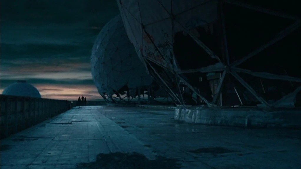 We Are The Night (2010) movie still: wide — A desolate concrete plateau features large, damaged geodesic domes marked by graffiti at dusk. The…