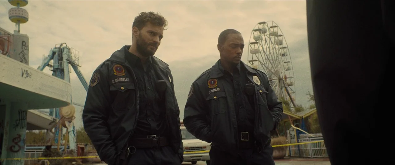 Synchronic (2019) movie still: medium — Two paramedics stand in an abandoned amusement park near a ferris wheel and rides. They look off-screen…