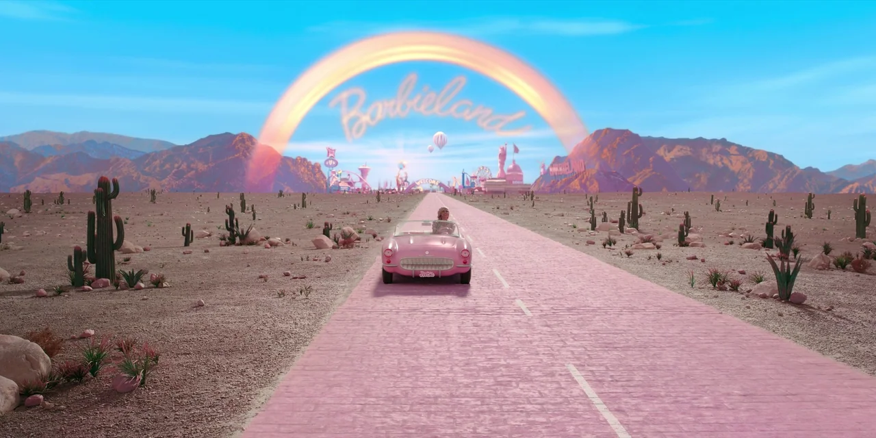 Barbie (2023) movie still: wide — A vast, pink-hued desert road leads toward a stylized city under a large rainbow. A single pink convertible car…