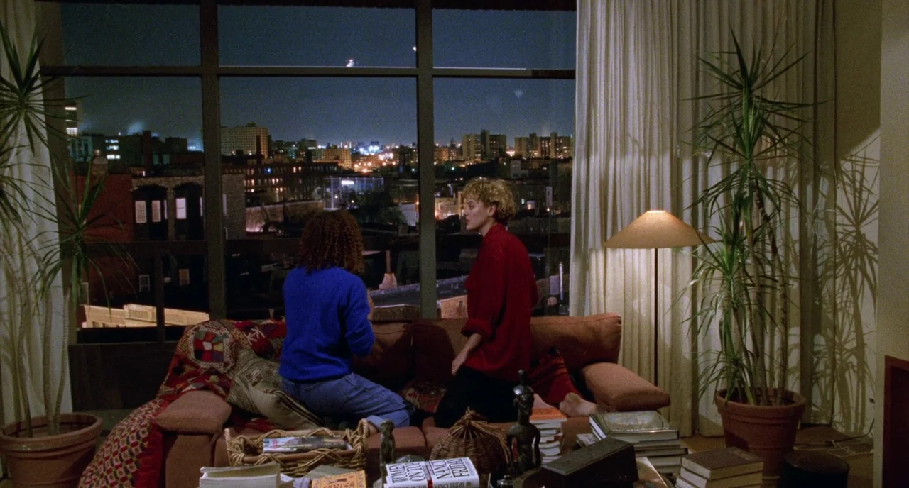 Candyman (1992) movie still: medium — A dimly lit room features a large floor-to-ceiling window overlooking a city skyline at night. Two women sit…