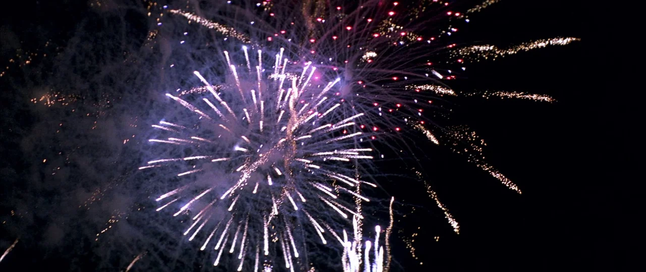 George Washington (2000) movie still: establishing — A night sky illuminated by multiple colorful exploding pyrotechnics. Sparkling light trails…