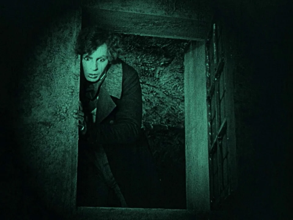 Nosferatu (1922) movie still: medium — A dark stone interior features a narrow rectangular doorway framed by rugged textures. A man in a dark coat…