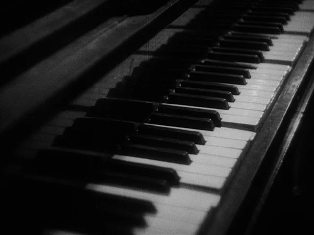 The Docks of New York (1928) movie still: closeup — A close up view of piano keys set against a dark background. Light illuminates the texture of…