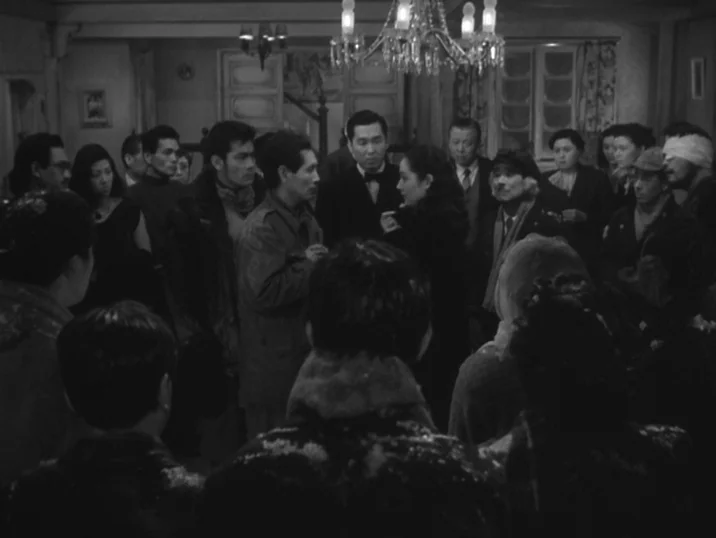 The Idiot (1951) movie still: medium — A crowded interior room with a large chandelier hanging from the ceiling. A diverse group of people in period…