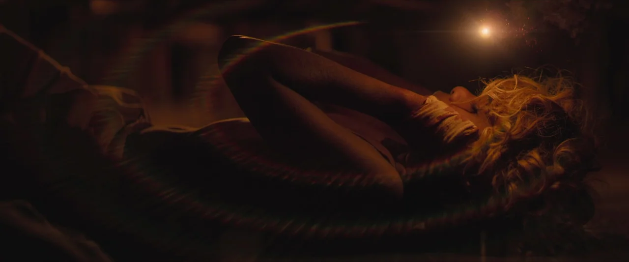 The New Boy (2023) movie still: closeup — A dimly lit, dark space shows a person resting on the ground. A woman with blonde hair lies on her side…